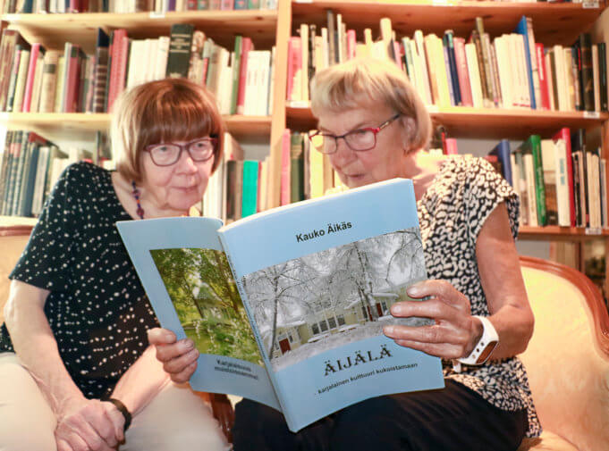 Arja Lehto ja Sirkka Vesterinen selailevat Kauko Äikkään painotuoretta kirjaa. Äikäs lahjoitti viime syksynä Äijälä-taloon liki 500 niteen kokoelmansa Karjala-aiheisia kirjoja. Teoksista vain osa näkyy kuvassa taustalla.