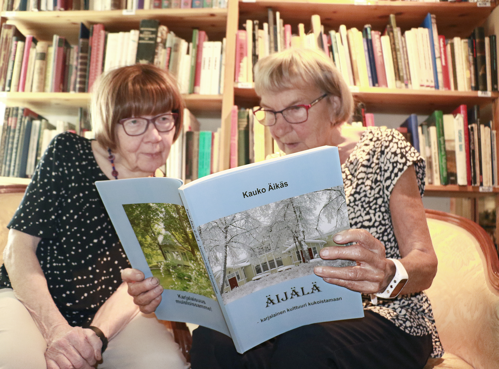 Arja Lehto ja Sirkka Vesterinen selailevat Kauko Äikkään painotuoretta kirjaa. Äikäs lahjoitti viime syksynä Äijälä-taloon liki 500 niteen kokoelmansa Karjala-aiheisia kirjoja. Teoksista vain osa näkyy kuvassa taustalla.